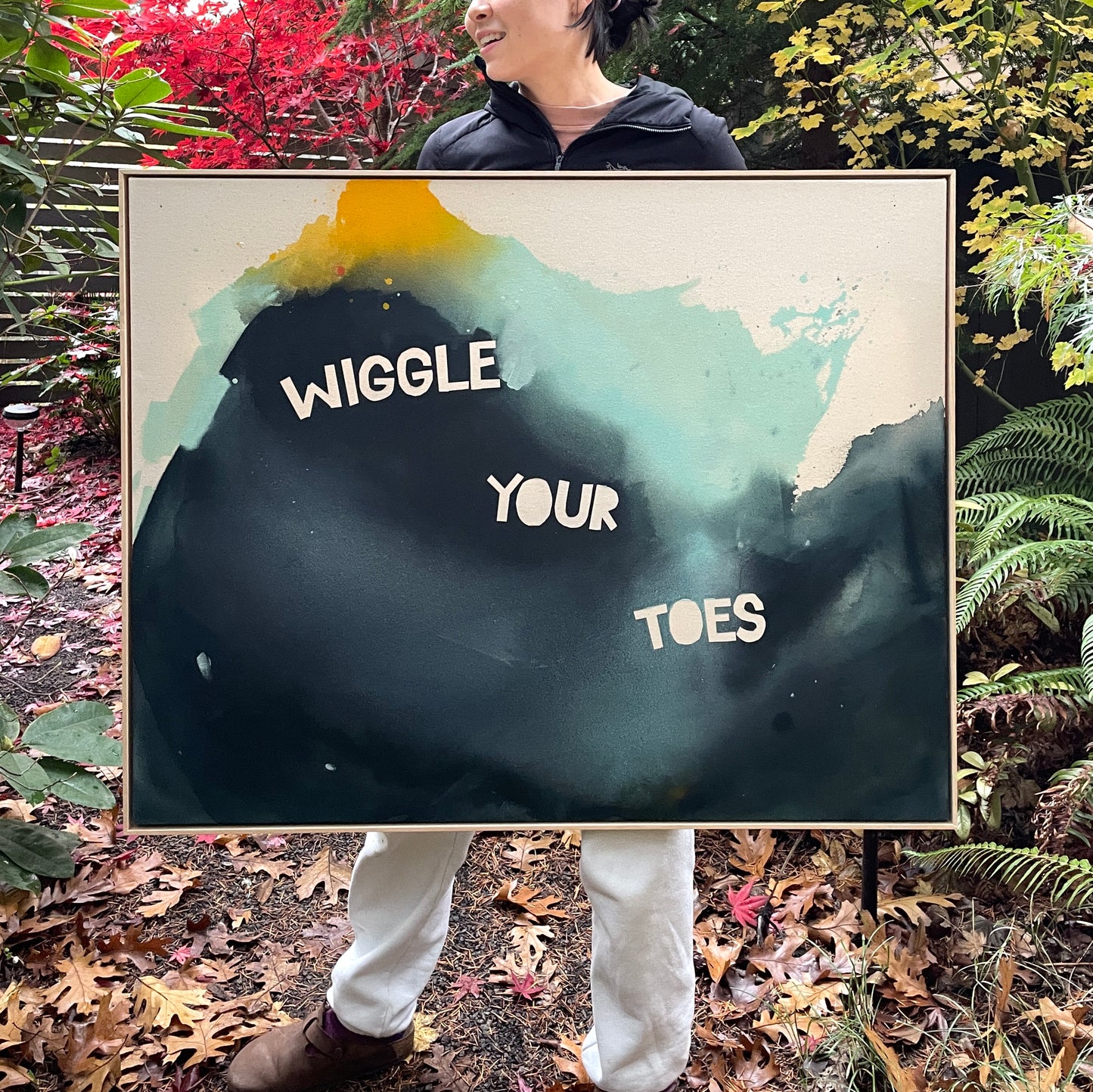 photo of person holding original painting by britchida showing navy, teal, yellow, and orange shapes with text "WIGGLE YOUR TOES"