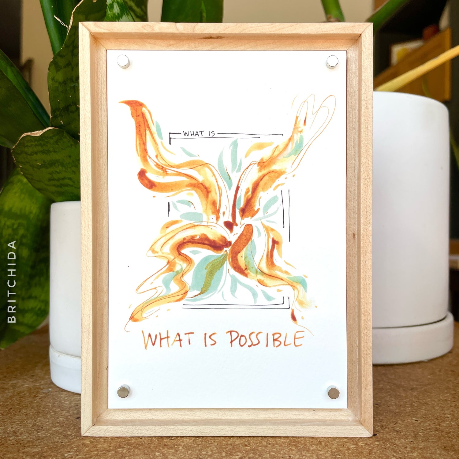 print "WHAT IS POSSIBLE" in wooden frame with 4 small silver magnets holding print in frame. plants can be seen in the background
