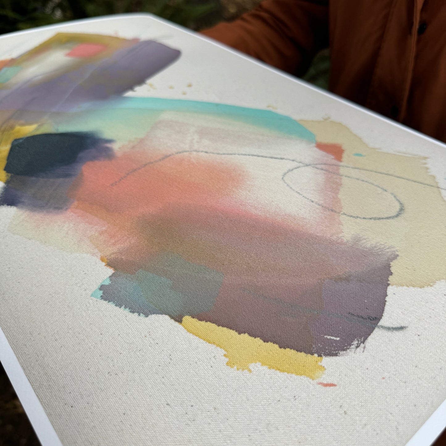 person in orange jacket holding print of abstract painting by britchida with yellow, teal, peach, navy, and lilac shapes with various thin lines