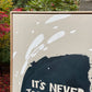 close up photo of original painting by britchida showing tan canvas with white and navy shapes and the block letters "IT'S NEVER"