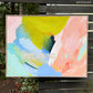 abstract painting by Britchida hanging on a wooden fence with various shapes of lime green, blue, pink, teal, and navy with negative block letters "IMPENDING JOY" revealing raw canvas underneath