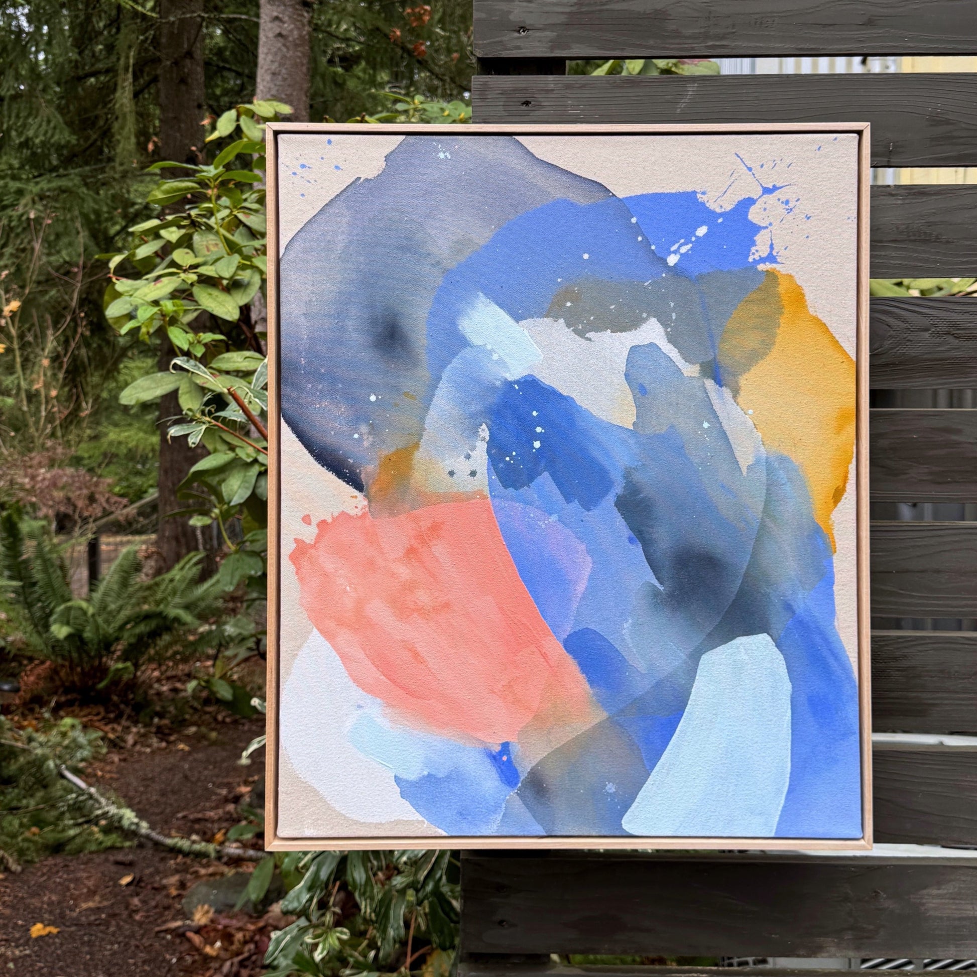 abstract painting by Britchida hanging on a wooden fence with various shapes of blue, ice blue, pink, yellow, and white