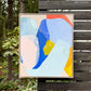 abstract painting by Britchida hanging on a wooden fence with various shapes of blue, periwinkle, yellow, orange, pink, and white