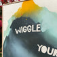 close up photo of original painting by britchida showing navy, teal, yellow, and orange shapes on canvas texture with wooden frame and words "WIGGLE YOUR"