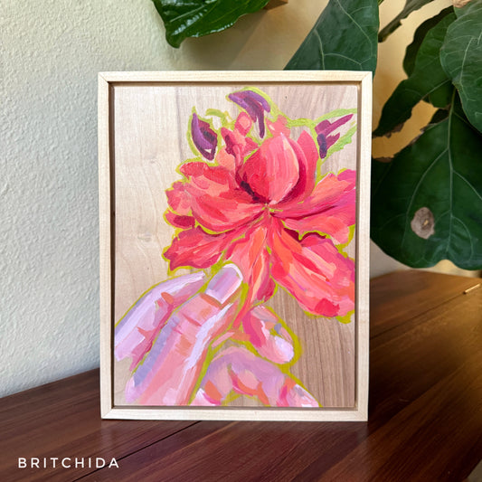 framed painting on wood of pink flower held by fingers by britchida