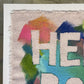 close up of print of rough edged raw canvas with bright multicolor marks on it with the words “HELLO BODY” masked out.