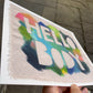 print of rough edged raw canvas with bright multicolor marks on it with the words “HELLO BODY” masked out.