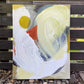 original abstract painting by britchida with yellow, gray, orange, and white shapes on canvas resting on an outdoor fence