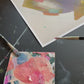 video of print of abstract painting by britchida with yellow, teal, peach, navy, and lilac shapes with various thin lines with paint palette in lower left corner