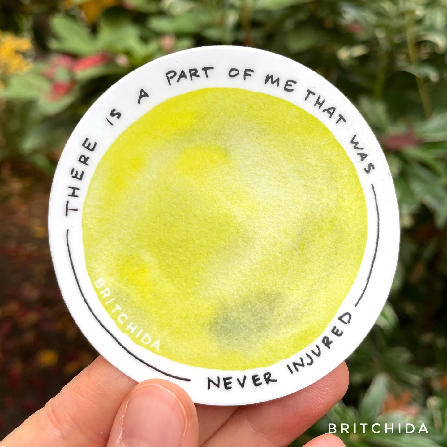 sticker of Never Injured print with a large yellow circle. around the circle is the text "there is a part of me that was never injured"