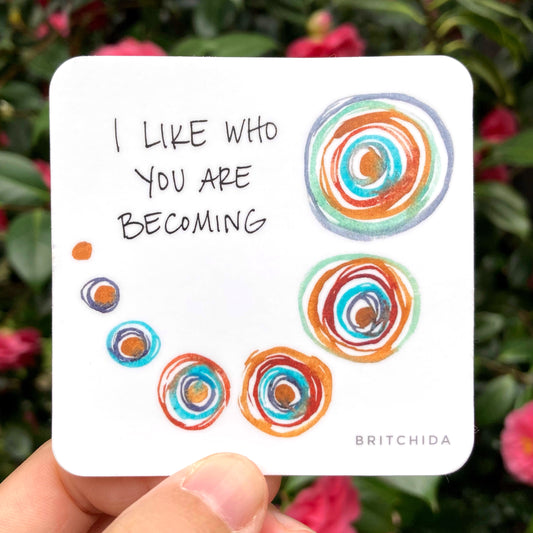 sticker of Becoming print with various circles increasing in size and number of concentric circles in different colors and the text "I like who you are becoming"