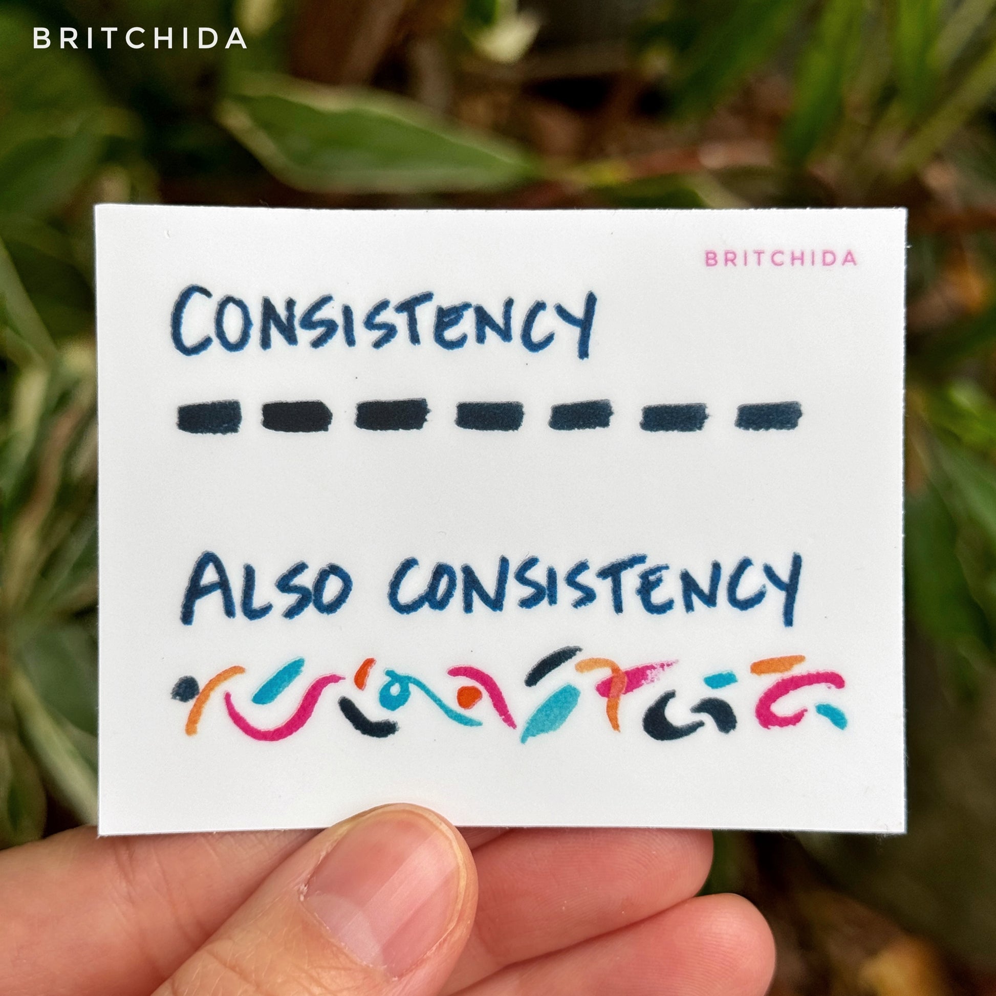 3" sticker of Consistency print. At the top are short black lines with the word "consistency". At the bottom are waves and shapes of orange, pink, blue, and black lines with the words "also consistency"