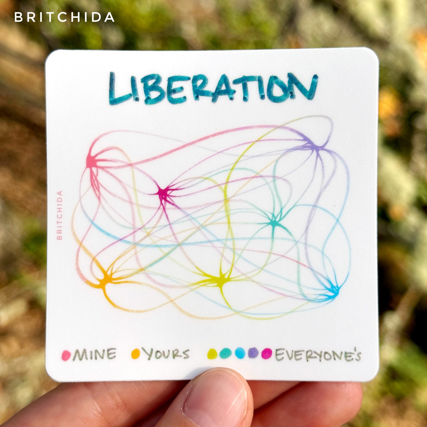 3" sticker of "Liberation" with connecting and weaving rainbow lines. The pink is labeled "mine"; the yellow is labeled "yours". There are green, teal, blue, purple, and pink dots that are labeled "everyone's"