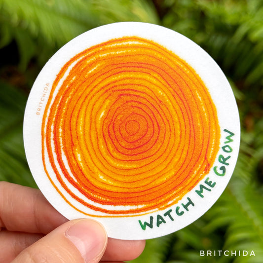 sticker for Watch Me Grow print. abstract painting of concentric circles like a cross section of a log with the text in green "watch me grow"