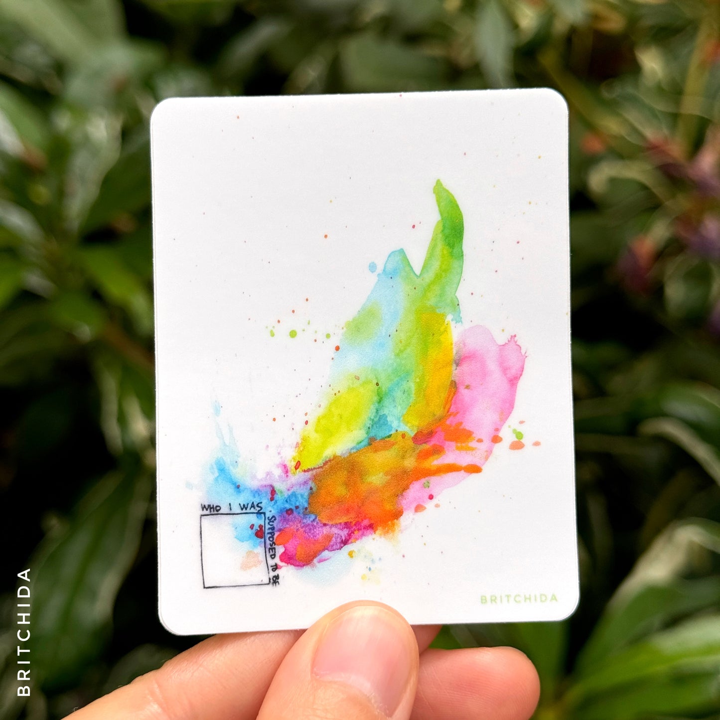 sticker of Who I Am print with a small box with black outline in bottom left corner and the words "who I was supposed to be". from the upper right corner is an explosion of rainbow paint colors that rise to the upper right corner