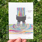 a stream of multi-colored fluid pouring through a black cauldron with two outlets (which sort of look like shorts) into a large pool below. The cauldron is labeled "The Binary" and the liquid labeled "Gender Fluid."