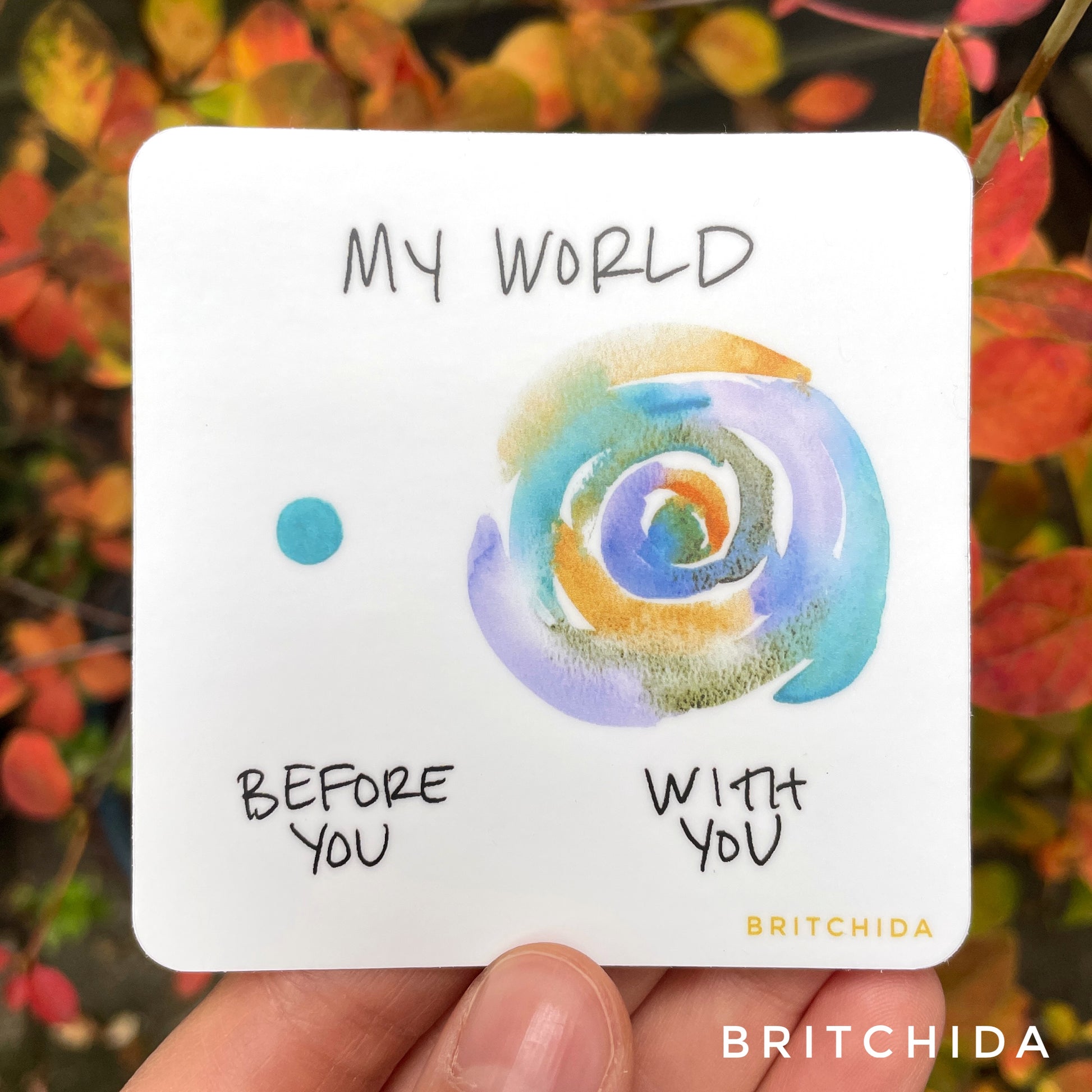 sticker of My World print with a single blue dot on the left with the text "before you" and a larger shape of concentric circles of blue, purple, and orange and the text "with you" below. At the top is the text "my world"